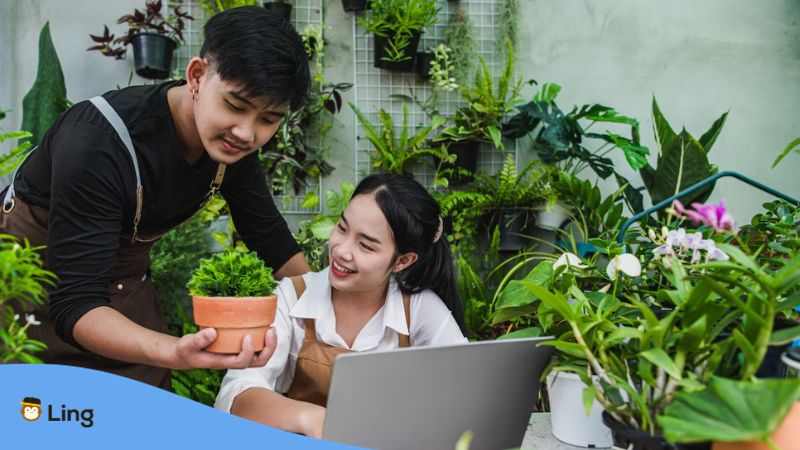A photo of two happy gardeners looking at a plan in a pot and using a laptop to search for Cantonese words for gardening.