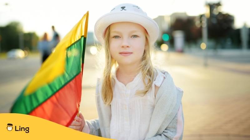 Litauische blondes Mädchen, mit Hut, hält die litauische Flagge in der Hand und fragt sich, welcher Name ist in Litauen am weitesten verbreitet? Erfahre mehr mit der Ling-App