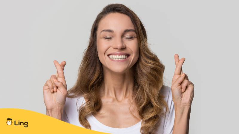 Junge blonde Frau kreuzt die Finger, um viel Glück auf Litauisch zu wünschen, mit der Ling-App gelernt