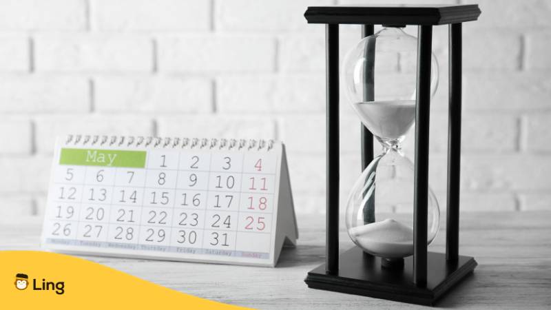 Tischkalender mit dem Monat Mai und Sanduhr vor hellem Hintergrund. Erfahre mehr über armenische Tage und Monate mit der Ling-App.