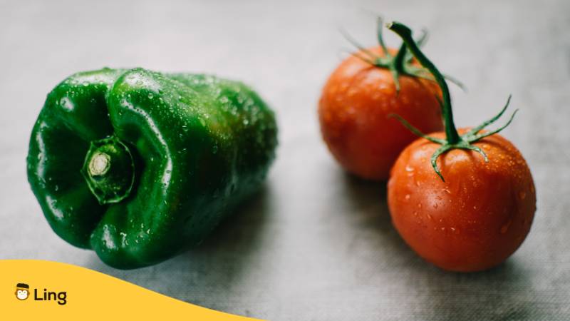 Eine grüne Paprika und zwei rote Tomaten liegen auf hellgrauer Fläche. Früchte, die du möglicherweise für Gemüse hältst.