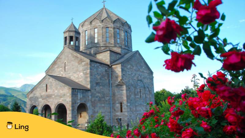 Armenische Kirche hinter einem Rosenstrauch. Lerne Armenisch und was schön auf Armenisch bedeutet mit der Ling-App.