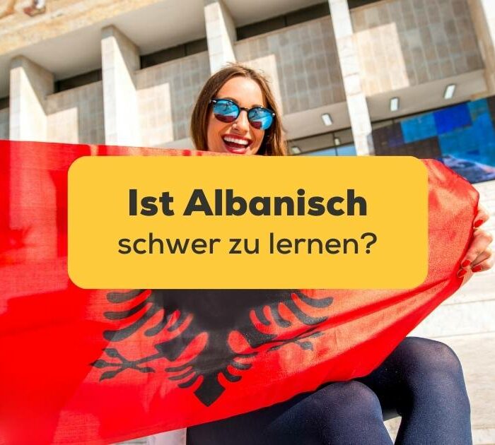 Junge Ling-App nutzerin sitzt mit großer albanischer Flagge vor Gebäude und trägt eine Sonnenbrille und lacht über die Frage Ist Albanisch schwer zu lernen?