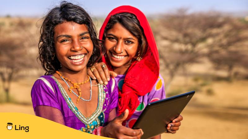 Glückliche junge indische Mädchen, die ein digitales Tablet benutzen, Wüstendorf, Indien. Lerne Malayalam Verben, um dein Malayalam mit der Ling-App zu verbessern.
