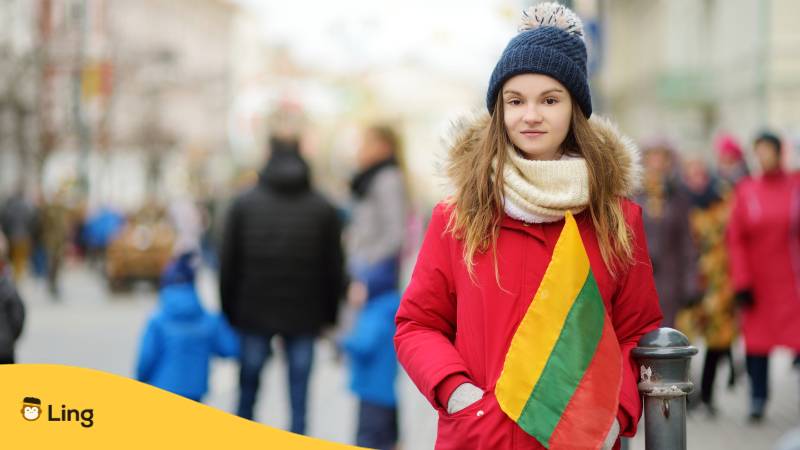 Junge litauische Frau in Winterkleidung hält eine litauische Flagge. Lerne wichtige litauische Übergangswörter mit der Ling-App.