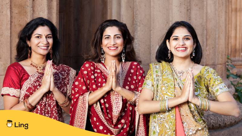Drei schöne indische Frauen in traditionellen Saris grüßen Namaste. Lerne herzliche Glückwünsche auf Malayalam auszudrücken mit der Ling-App.