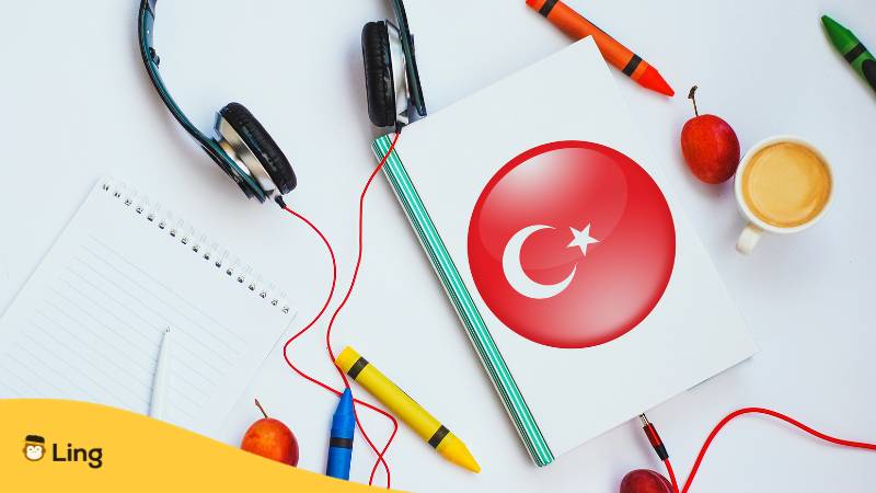 Buch mit türkischer Flagge und Kopfhörer. Konzept des türkisch Lernens durch Audiokurse. 
Lerne türkische Umgangssprache und 20 türkische Slang-Wörter, die jeder Muttersprachler verwendet. Lerne Türkisch mit der Ling-App.