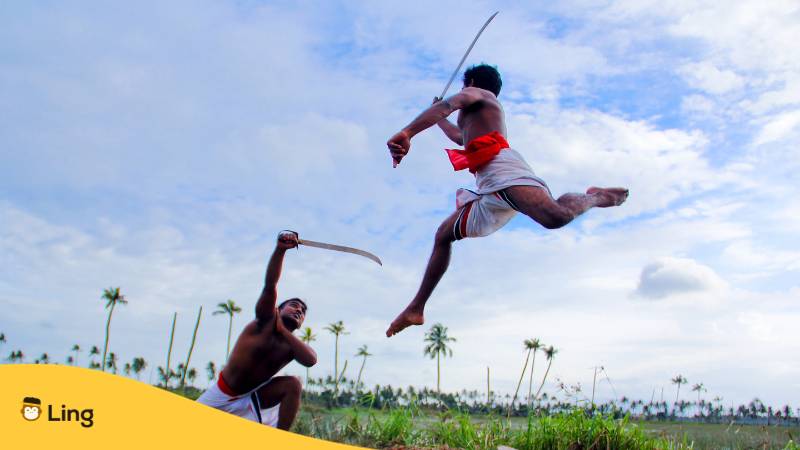 Zwei Männer in weißen Shorts kämpfen tagsüber mit einem Schwert. Erfahre mehr über Malayalam Adjektive mit der  Ling-App.