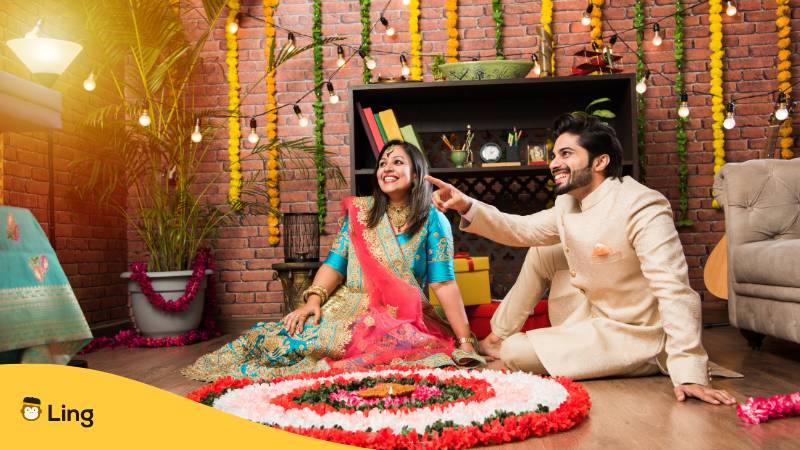 Indisches Paar, das an Diwali oder Onam Blumen-Rangoli macht, ein Selfie macht oder Süßigkeiten hält. Lerne mit der Ling-App Traditionen und Rituale in Kerala kennen.
