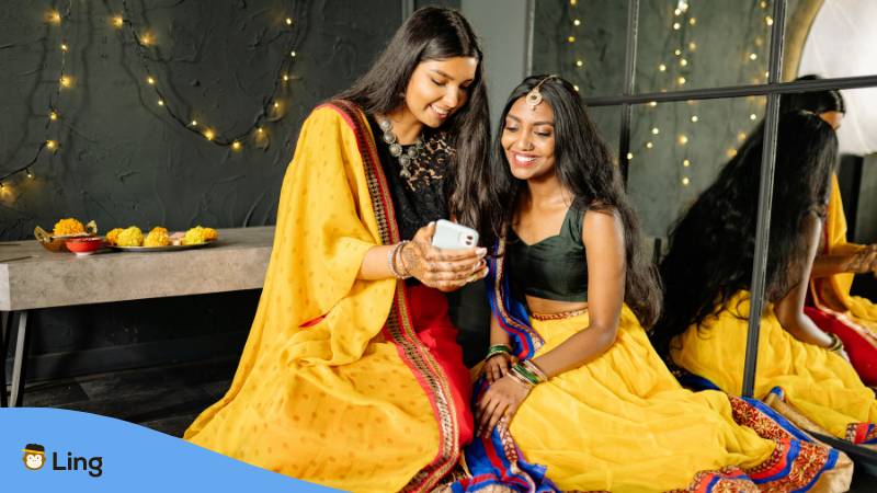 Zwei indische Frauen in traditioneller Kleidung schauen sich die Ling-App an und lesen - Wie lange dauert es Malayalam zu lernen? - Lerne auch du Malayalam mit der Ling-App.