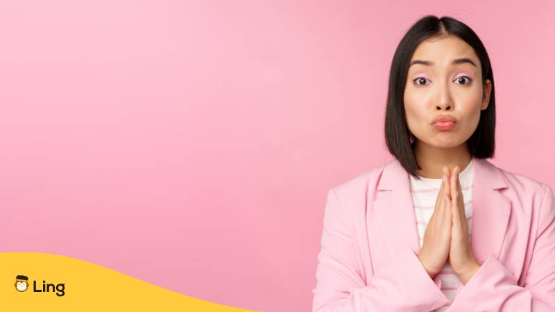 Porträt einer asiatischen Geschäftsfrau, die um Hilfe bittet, in betender, flehender Pose stehend, rosa Studiohintergrund. Lerne 3 einfache Wege, wie du höflich bitte auf Tagalog sagst mit der Ling-App.
