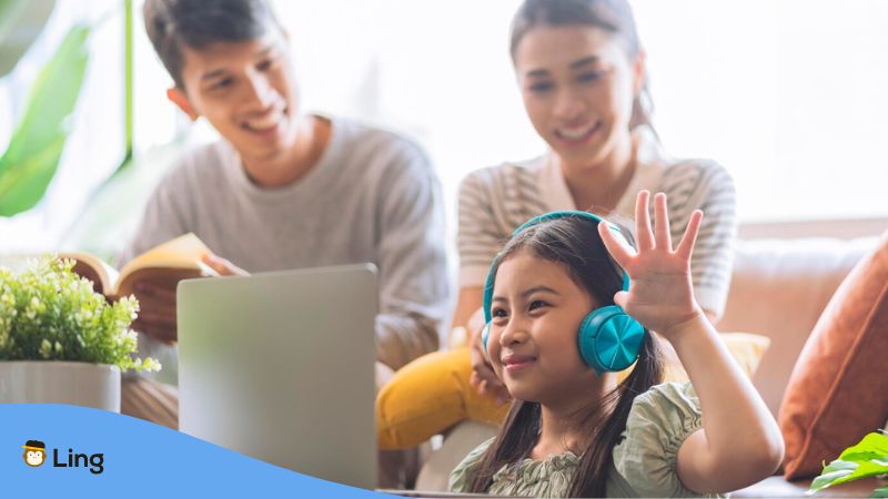 French online classes - A photo of a young girl raising hand in front of computer with parents.