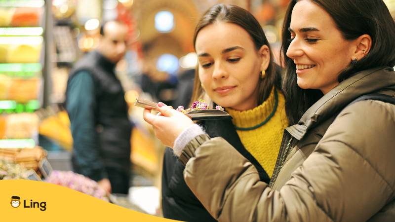 Zwei türkische Frauen schauen sich Waren auf einem türkischen Basar an. Lerne 100 einfache Sätze auf Türkisch für Touristen mit der Ling-App.