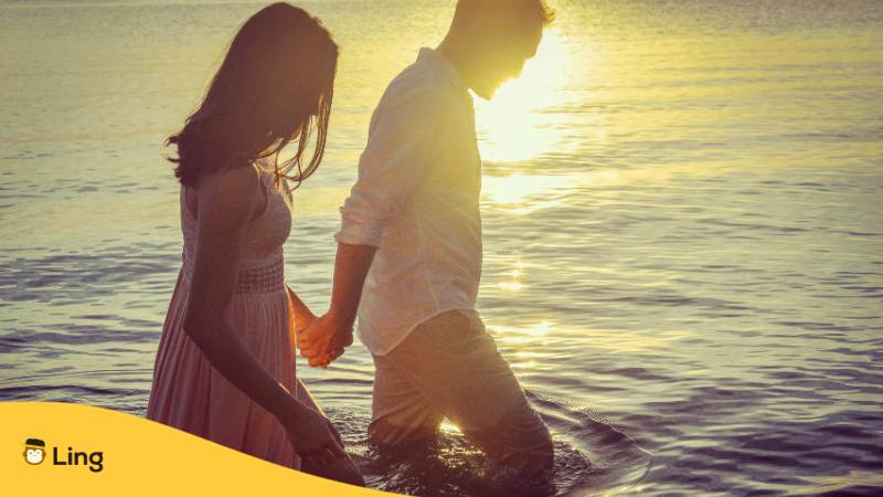 Paar läuft bei Sonnenuntergang Hand in Hand. Lerne 31 Verrückt süße Tagalog Liebesphrasen mit der Ling-App.
