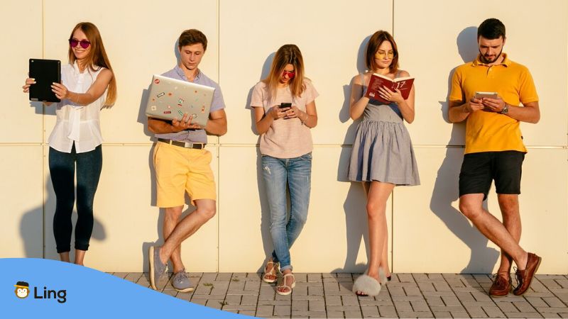 academic language learning apps - A photo of standing young people holding their books and gadgets.