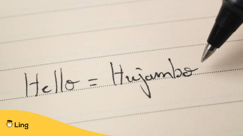 Swahili-Anfängerin, die das Wort Hujambo als Hausaufgabe auf ein Notizbuch schreibt, Makroaufnahme. Ist Swahili schwer zu lernen? Entdecke 5 faszinierende Wahrheiten! mit der Ling-App.
