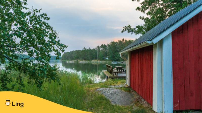 Blick auf finnischen See, auf der rechten Seite steht eine finnische Holzhütte. Erfahre in diesem Beitrag, warum es kein Finnisch bei Babbel gibt? Probier stattdessen doch einfach mal diese 2  Optionen aus!

