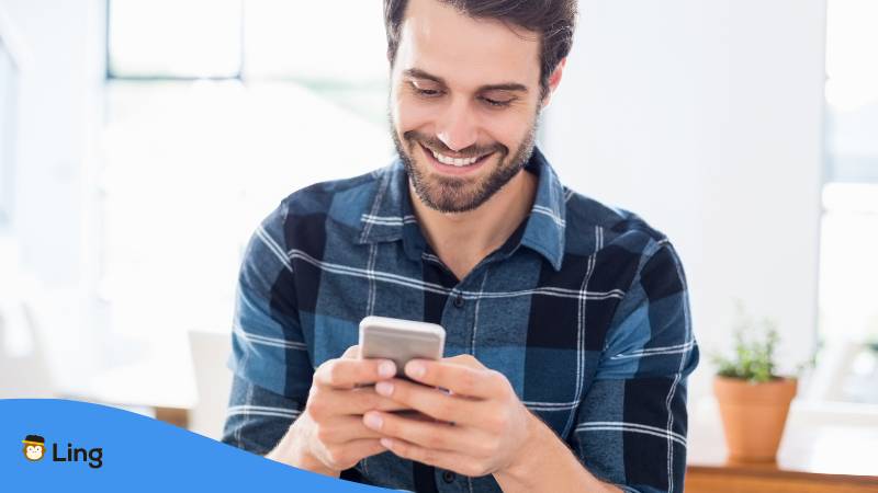 Mann freut sich und lächelt während er in sein Handy schaut, denn obwohl es kein Slowenisch auf Duolingo gibt kann er mit Ling Slowenisch lernen