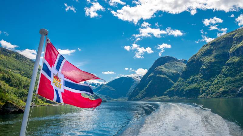 Norwegen - Die norwegische Flagge weht über dem Wasser. Entdecke die 10 die besten Wege Norwegisch zu lernen!