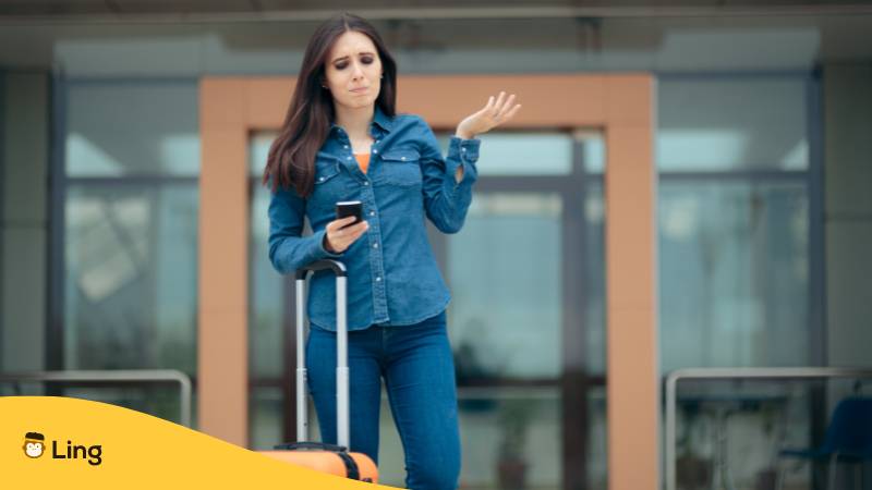 Reisende Frau hält Smartphone und fühlt sich im Flughafen verloren. Lerne über 40 Sätze für Notfälle auf Georgisch mit Ling!