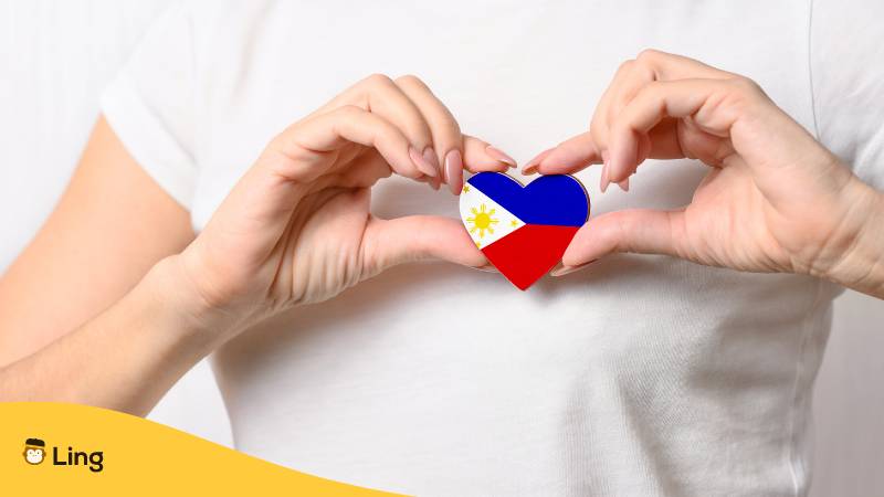 Frau hält ein Herz mit der Flagge der Philippinen an ihre Brust. Lerne über 14 beliebte Tagalog Verben und werde zum Sprachprofi!