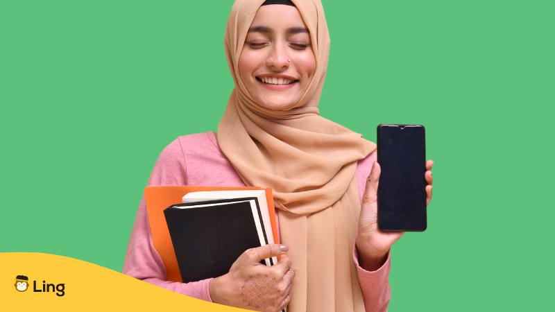 Pakistani Frau hält Bücher und ihr Handy in der Hand und freut sich und ist dankbar über die Ling-App mit der sie Urdu lernen kann