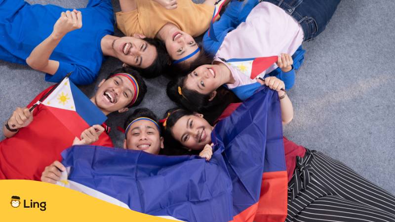 Menschen halten die philippinische Flagge zur Feier des Unabhängigkeitstages. Lerne die 3 besten Methoden um Farben auf Tagalog zu Lernen!


