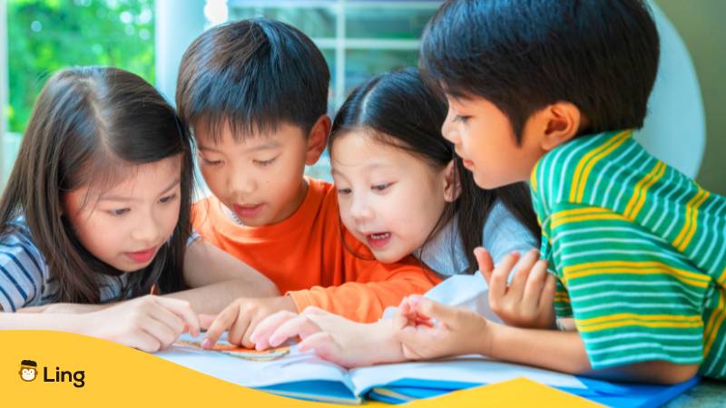 Asiatische kleine Kinder lesen Buch fröhlich. Erfahre alles über den Kindertag in Thailand mit der Ling-App!
