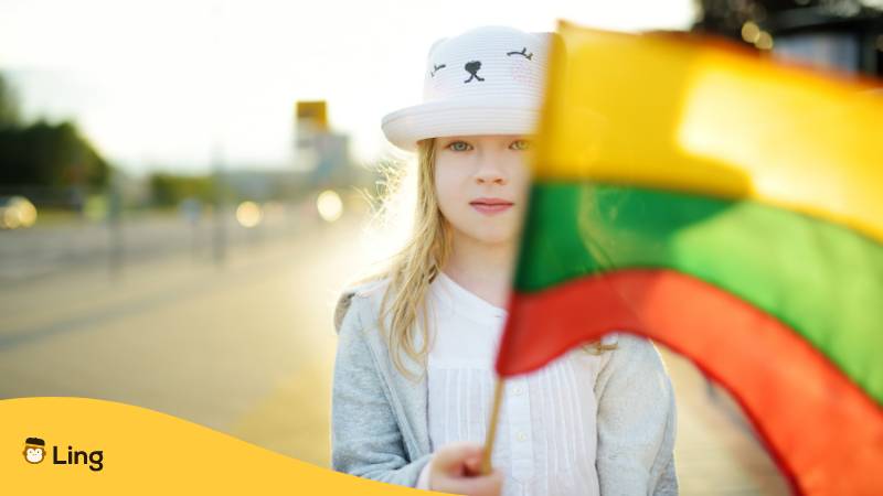 Mädchen hält eine litauische Flagge an einem sonnigen Frühlingstag. Lerne 20+ nützliche litauische Vokabeln für Wetter auf Litauisch!
