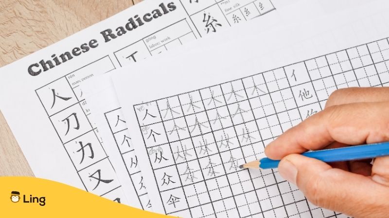 Hand holding pencil practicing Chinese characters on exercise sheet 