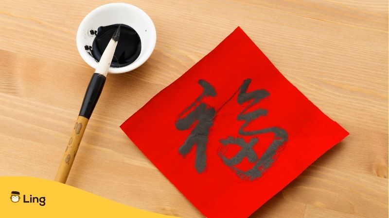 Chinese writing on a red piece of paper with brush and ink next to it