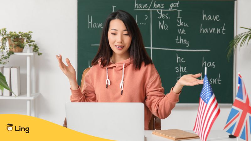 Female teacher using computer with blackboard behind. 