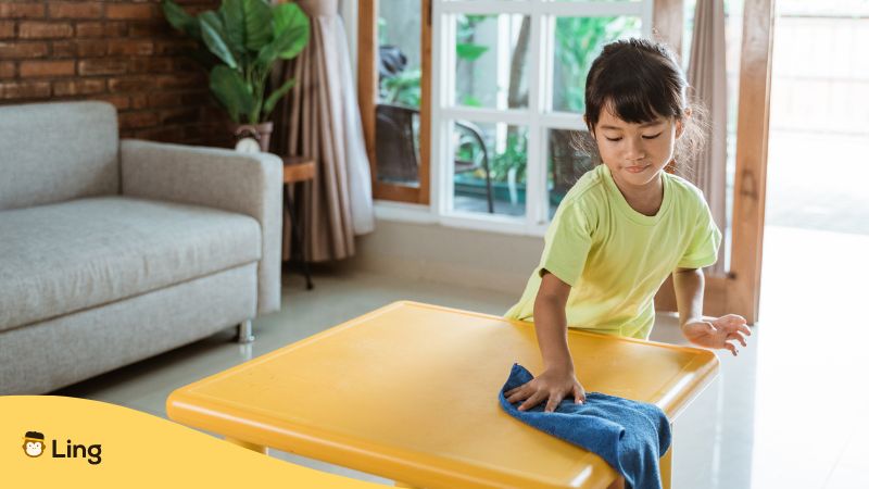 A kid wiping her table with a microfiber towel.