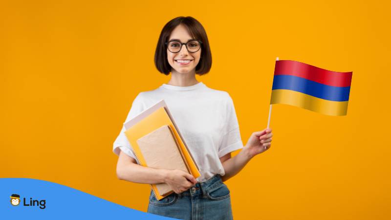 Lächelnde Frau mit Notebooks und kleine armenischer Flagge, Orange Hintergrund. Lerne über 5 wichtige Kategorien zu armenische Pronomen.

