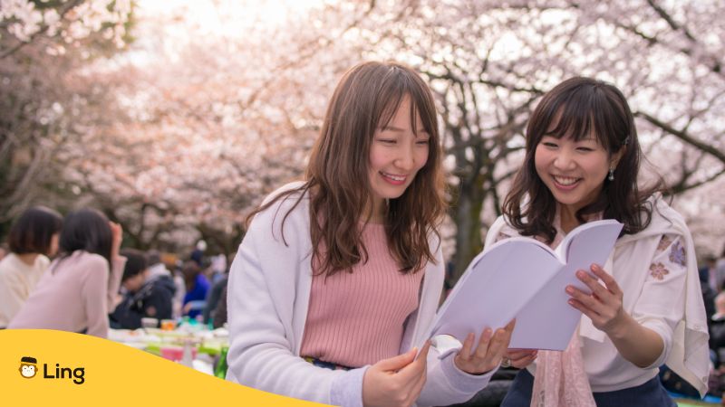 Young women reading book in hanami party