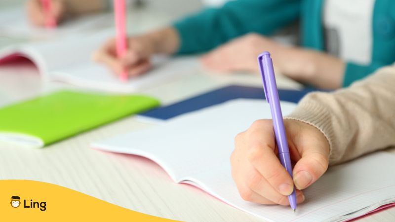 Students writing on notebooks with purple and pink pens.