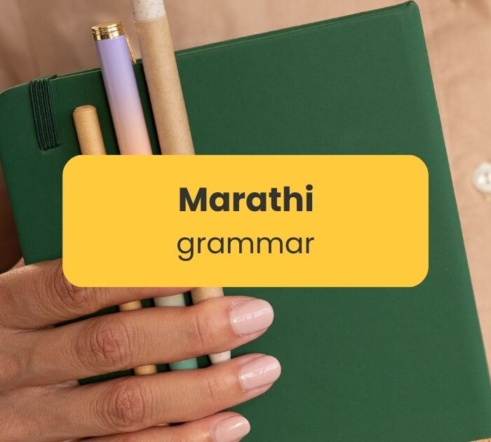 Hand holding notebook and pens - Marathi grammar