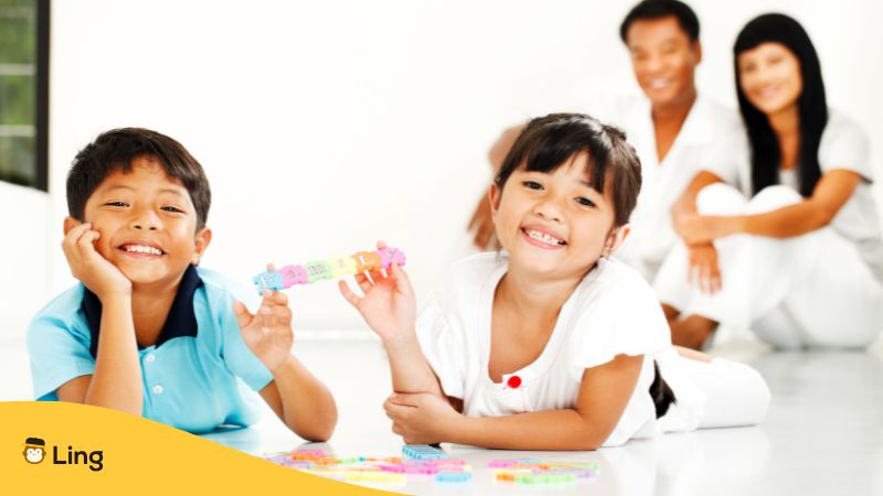 Two Thai Kids Playing On The Floor With Parents Watching Behind