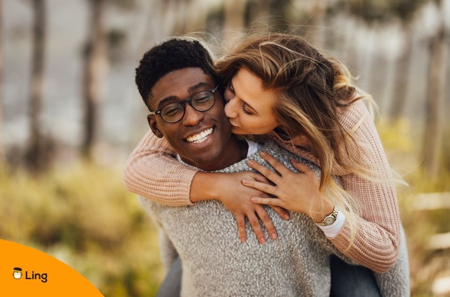 Interracial Couple With A Man Carrying A Woman On His Back As She Kisses His Cheek