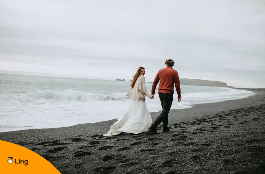 A Man And A Woman Walking And Holding Hands On A Beach In Iceland
