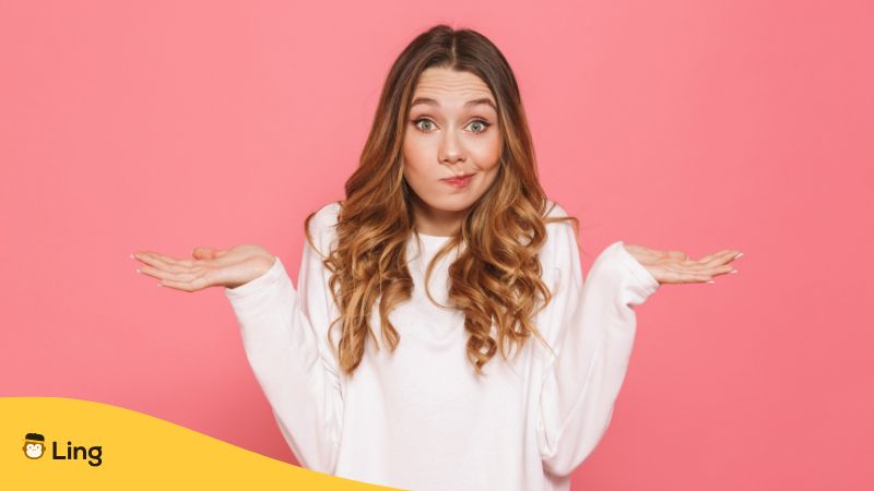 Portrait Of A Confused Woman With Brown Wavy Hair Shrugging Her Shoulders Against A Pink Background