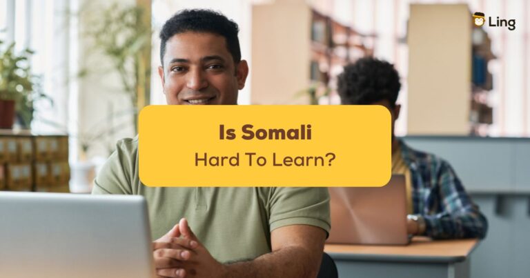An Adult Male Student Smiling At The Camera While Sitting At A Desk With Laptop And Studying Foreign Languages With Other Migrant Students In The Background - Is Somali Hard To Learn