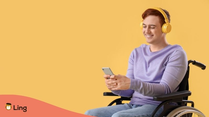 Hombre Joven En Silla De Ruedas Sonriendo, Usando El Celular Para Aprender Un Idioma