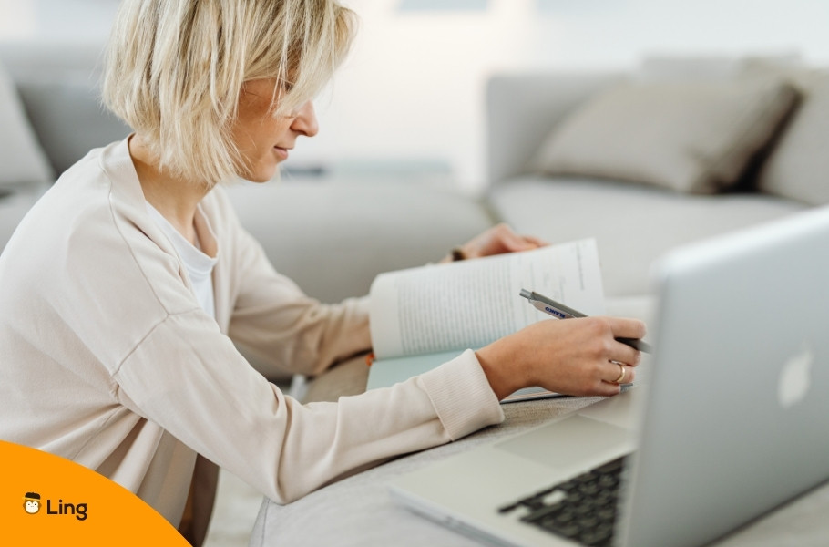 A Woman Learning Serbian On An Online Course On Her Laptop With The Help Of A Book