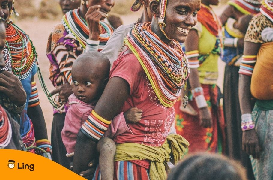Woman Wearing Colorful Clothes And Beads Carrying A Child On Her Back