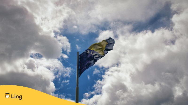 Die Bosnische Flagge Weht Vor Einem Bewölkten Himmel, Der Gerade Aufreißt.